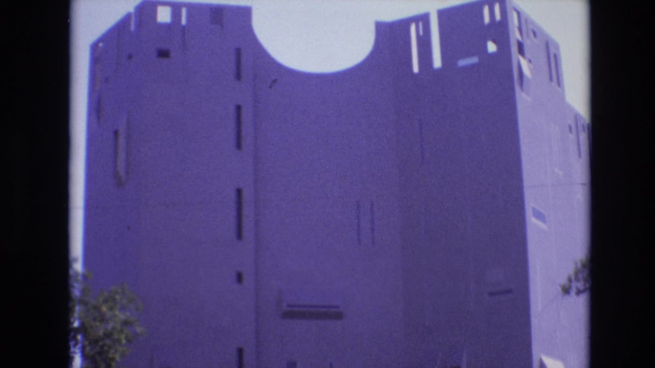 1974 Denver home-movie frame of a tall concrete building with a large semi-circular roof cutout, slit-like windows, and dark film-edge shadows.