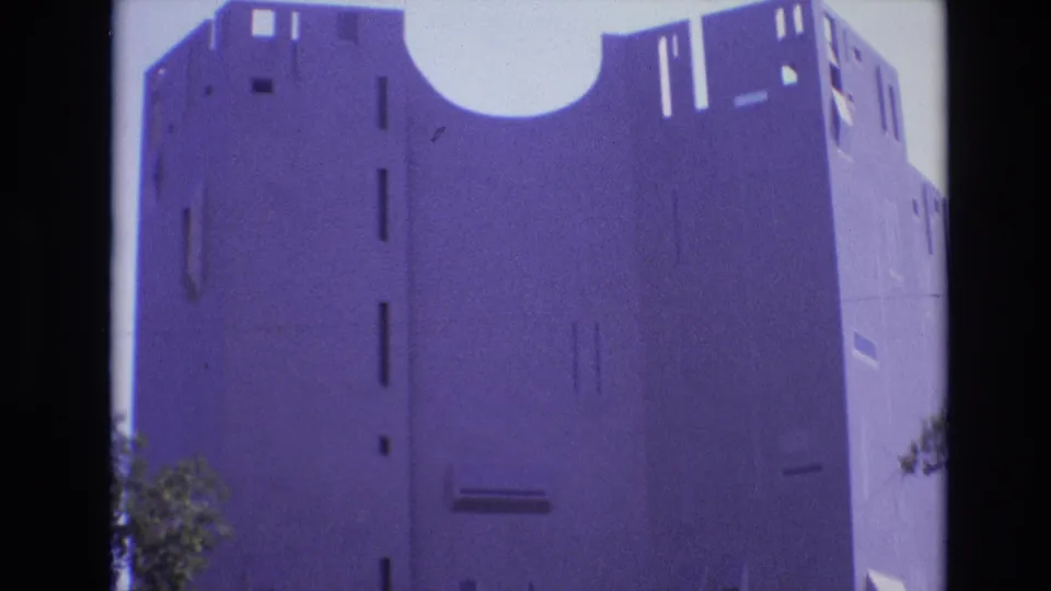 1974 Denver home-movie frame of a tall concrete building with a large semi-circular roof cutout, slit-like windows, and dark film-edge shadows.