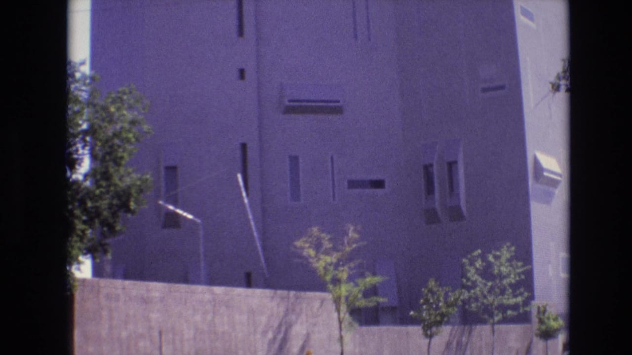 1974 Denver 8mm frame of a modernist exterior with a concrete wall, young trees, and streetlight, tinted by aged film color shifts.