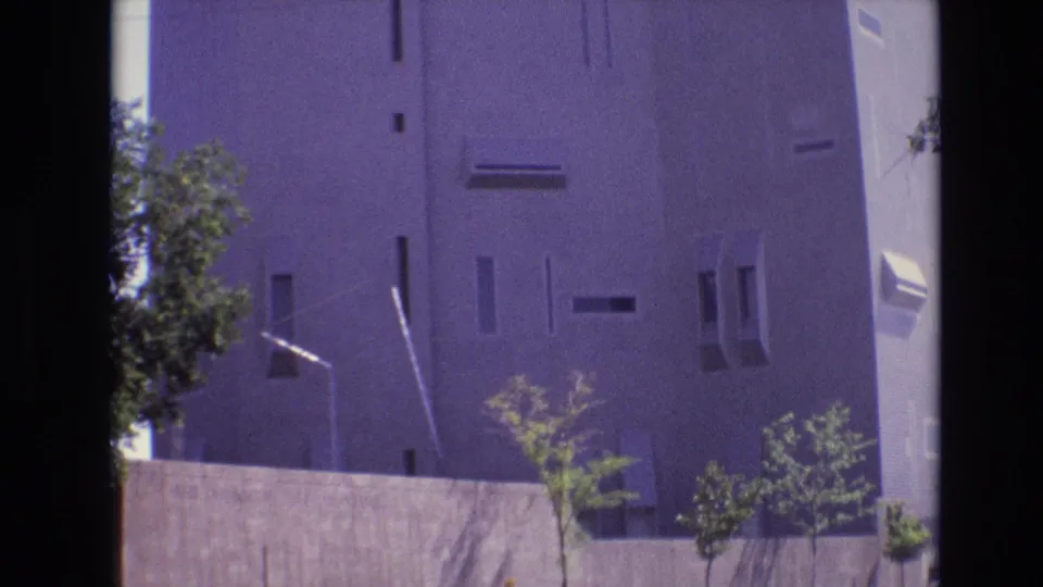 1974 Denver 8mm frame of a modernist exterior with a concrete wall, young trees, and streetlight, tinted by aged film color shifts.