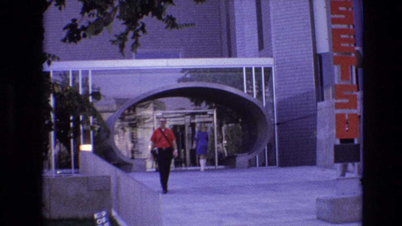 Man in red continues walking forward as a woman in blue approaches the entrance behind him.