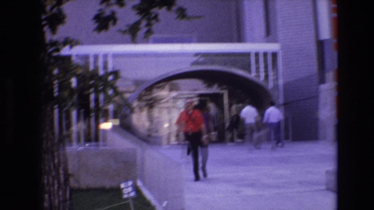 Pedestrian walking on a city sidewalk near a modern building entrance.