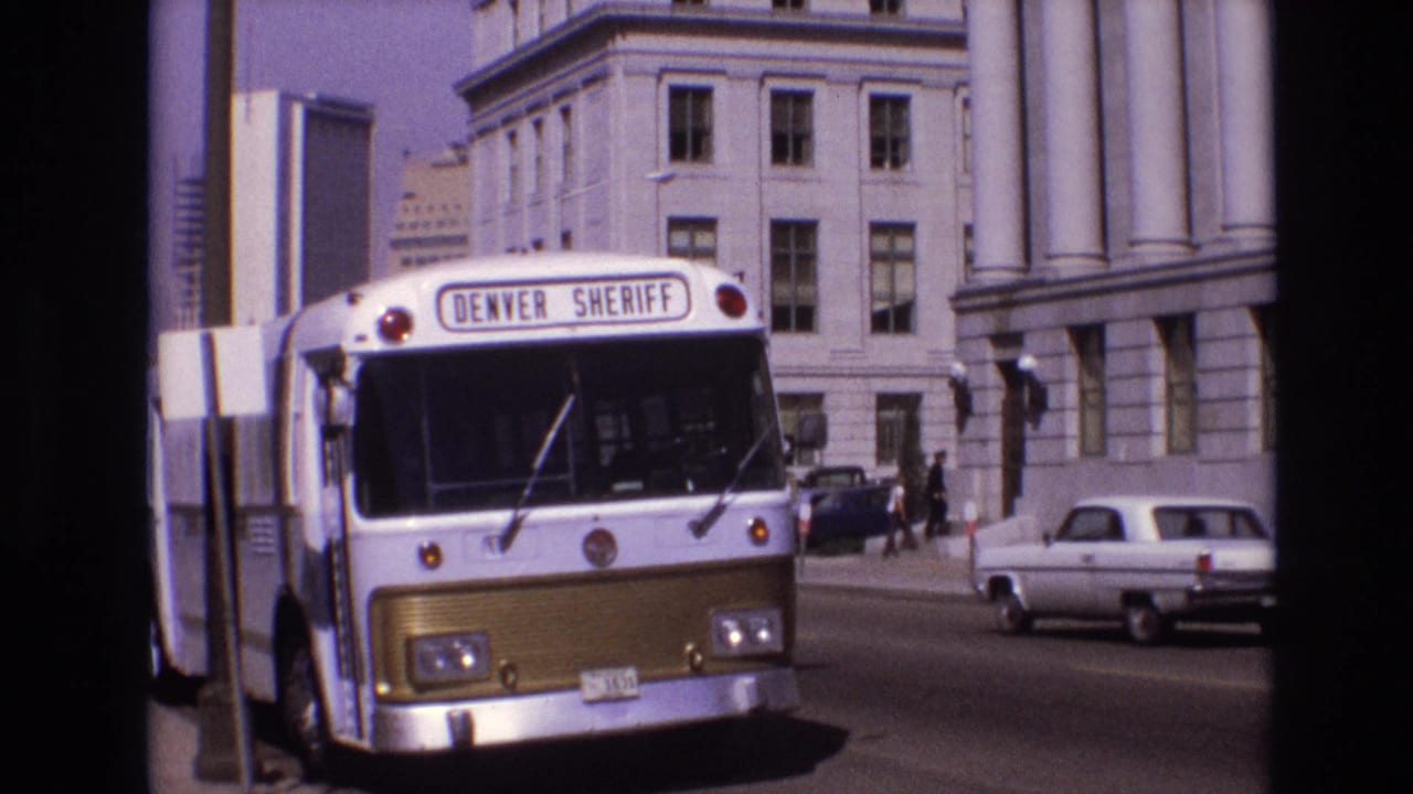 Denver Sheriff bus parked along a city street beside columned buildings.