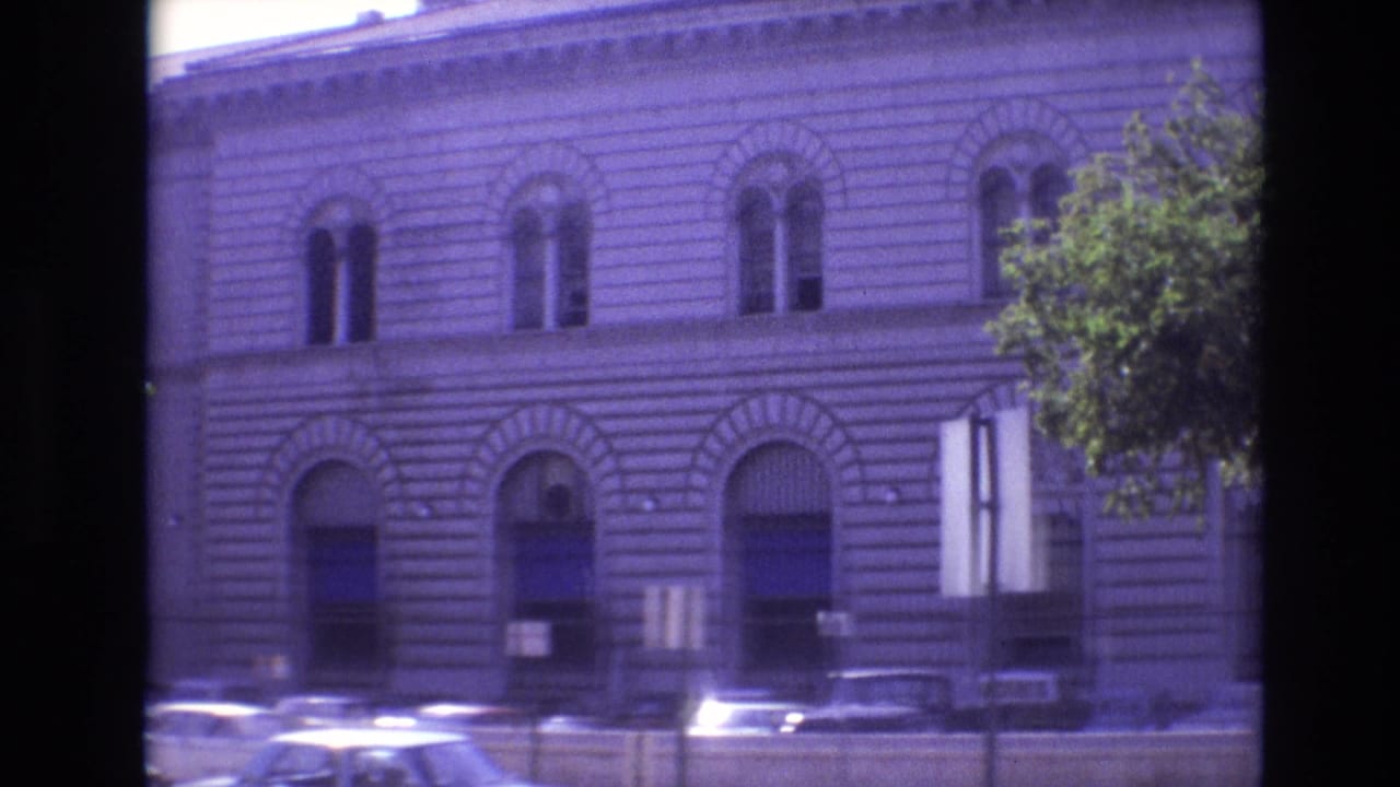 Stone building facade with arched windows and cars parked along the street.