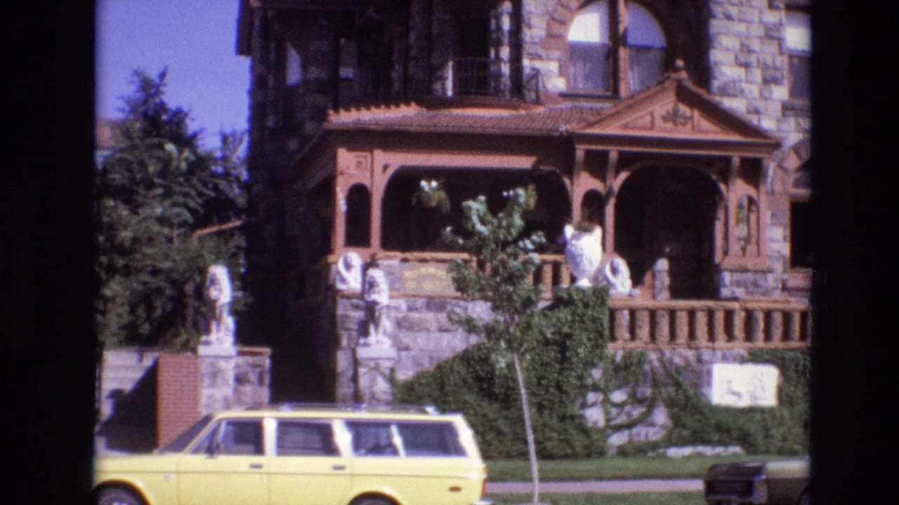 Wood porch and stone facade behind a yellow station wagon, with statues and greenery near the entrance.