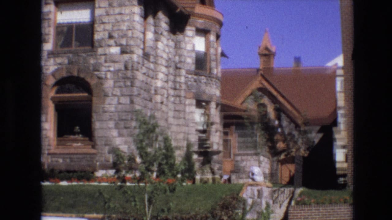 Stone house corner with turret-like wall, arched doorway, fountain, hedge, lawn, and side porch.