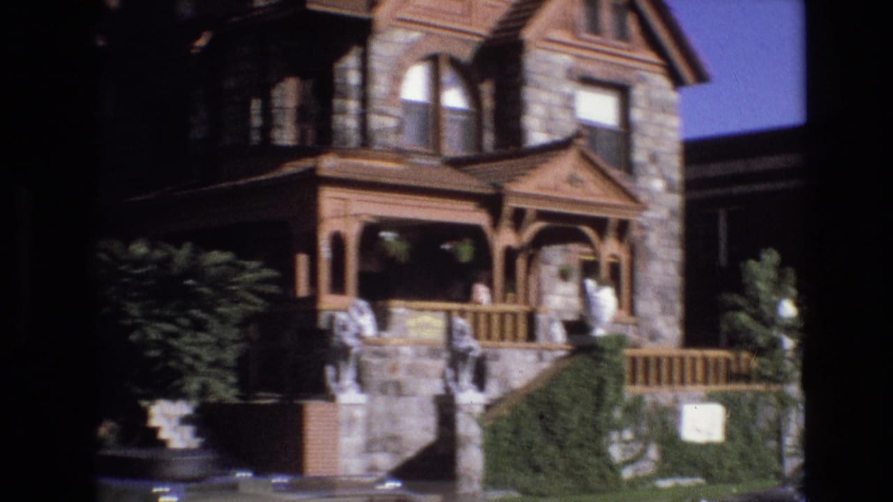 Stone and wood house with porch, steps, shrubs, and people near the entrance.