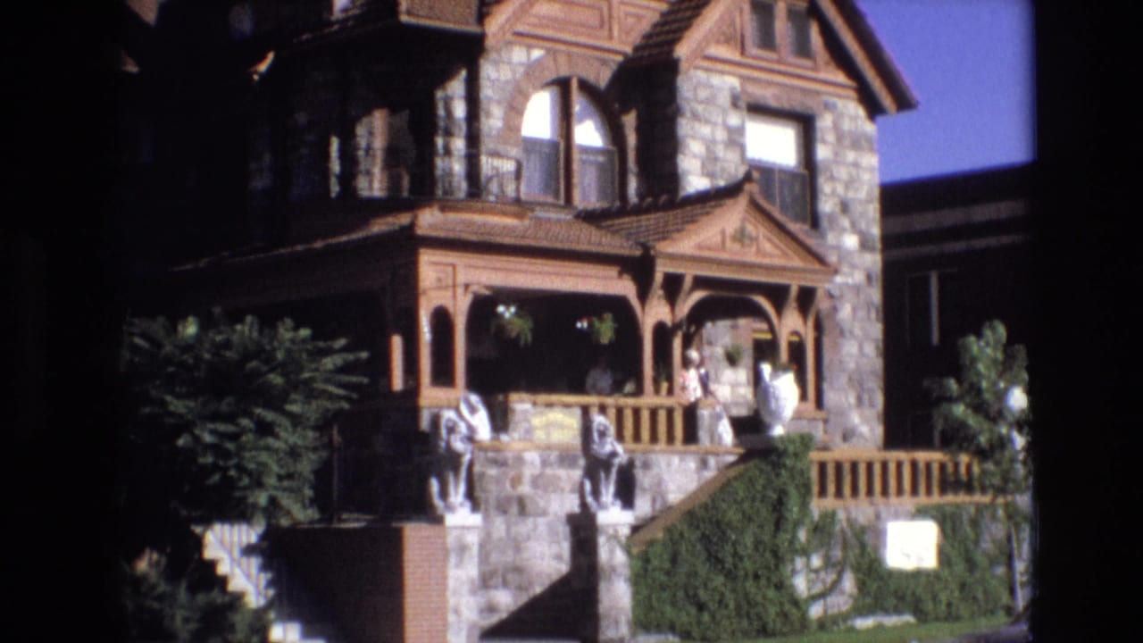 Front porch of a stone house with people standing near the doorway and steps.