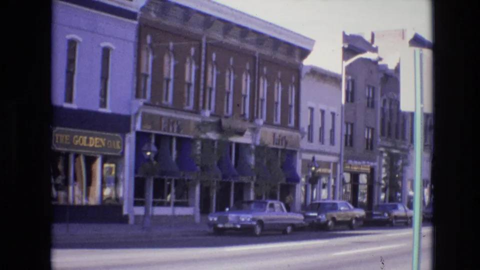 1974 Denver downtown storefront view with The Golden Oak sign, blue awnings, brick facades, and classic cars parked along the curb.