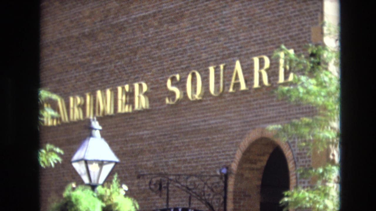 1974 Denver 8mm frame showing a brick Larimer Square facade with gold lettering, a gas-style lamp, an arched doorway, and green foliage.