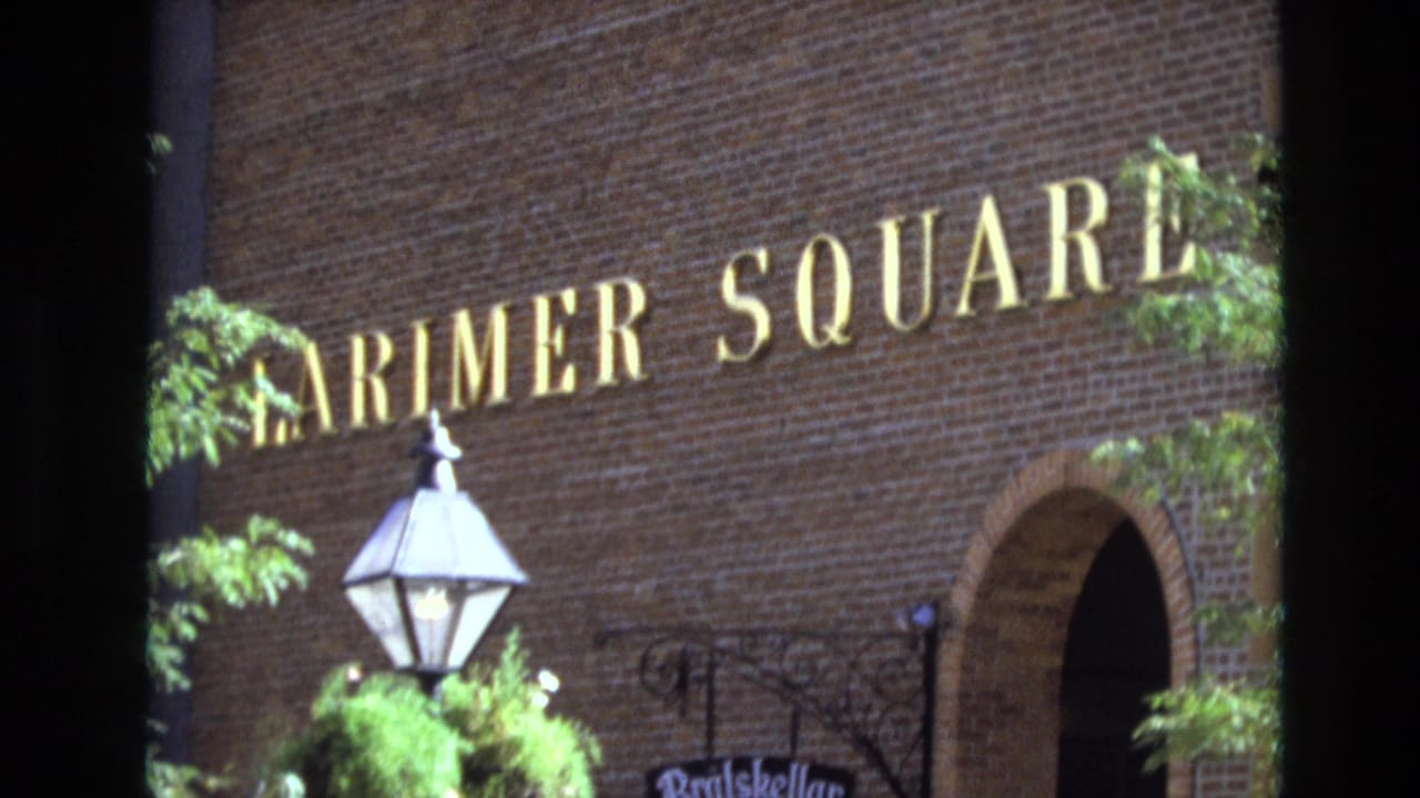 1974 Denver frame with Larimer Square lettering on a brick exterior, framed by foliage, a lamp, an arched entrance, and wrought iron trim.