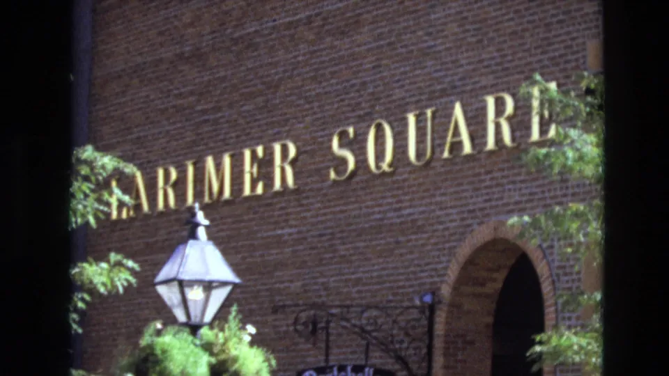 1974 Denver frame showing the Larimer Square sign on a brick building, with a gas-style lamp, foliage, wrought iron detail, and a dark arched entrance.