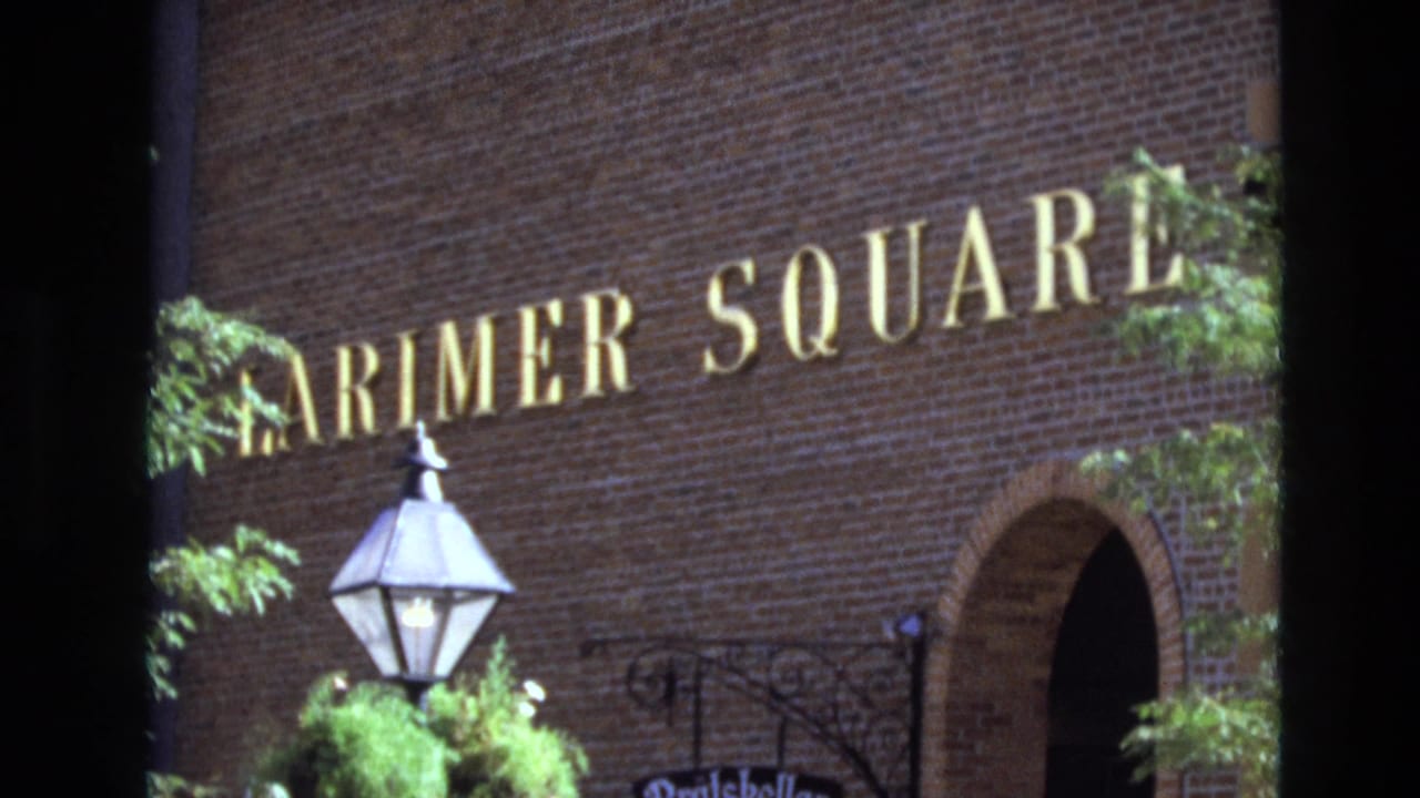 Brick wall with large Larimer Square lettering, lantern post, plants, and arched doorway.