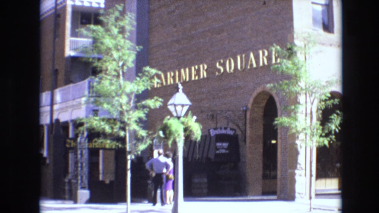 Larimer Square brick building with lantern post, trees, arched doorway, and two pedestrians near the entrance.