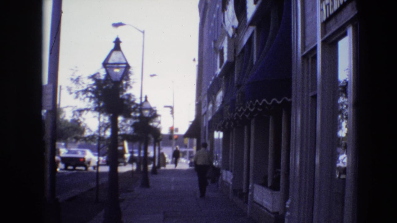 Similar sidewalk view with storefront awnings, street lamps, cars, trees, and pedestrians in the distance.