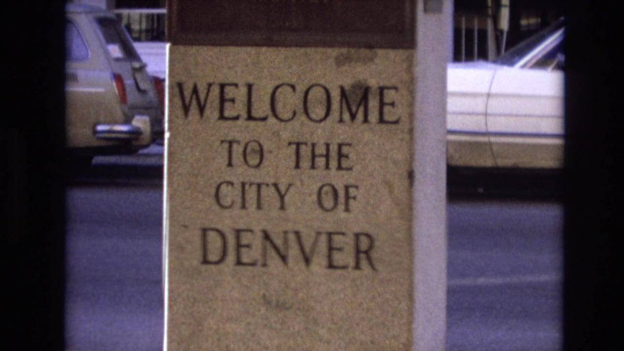 A similar 1974 Denver close-up holds on the stone city welcome sign, with a station wagon and white car partly visible behind it.