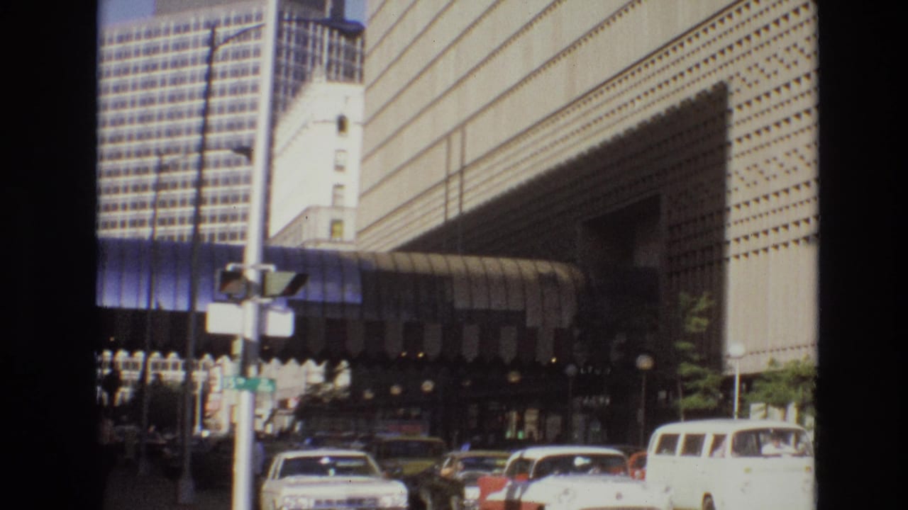 1974 Denver street-level view of cars and pedestrians near a striped awning and a large modernist building with a perforated facade.