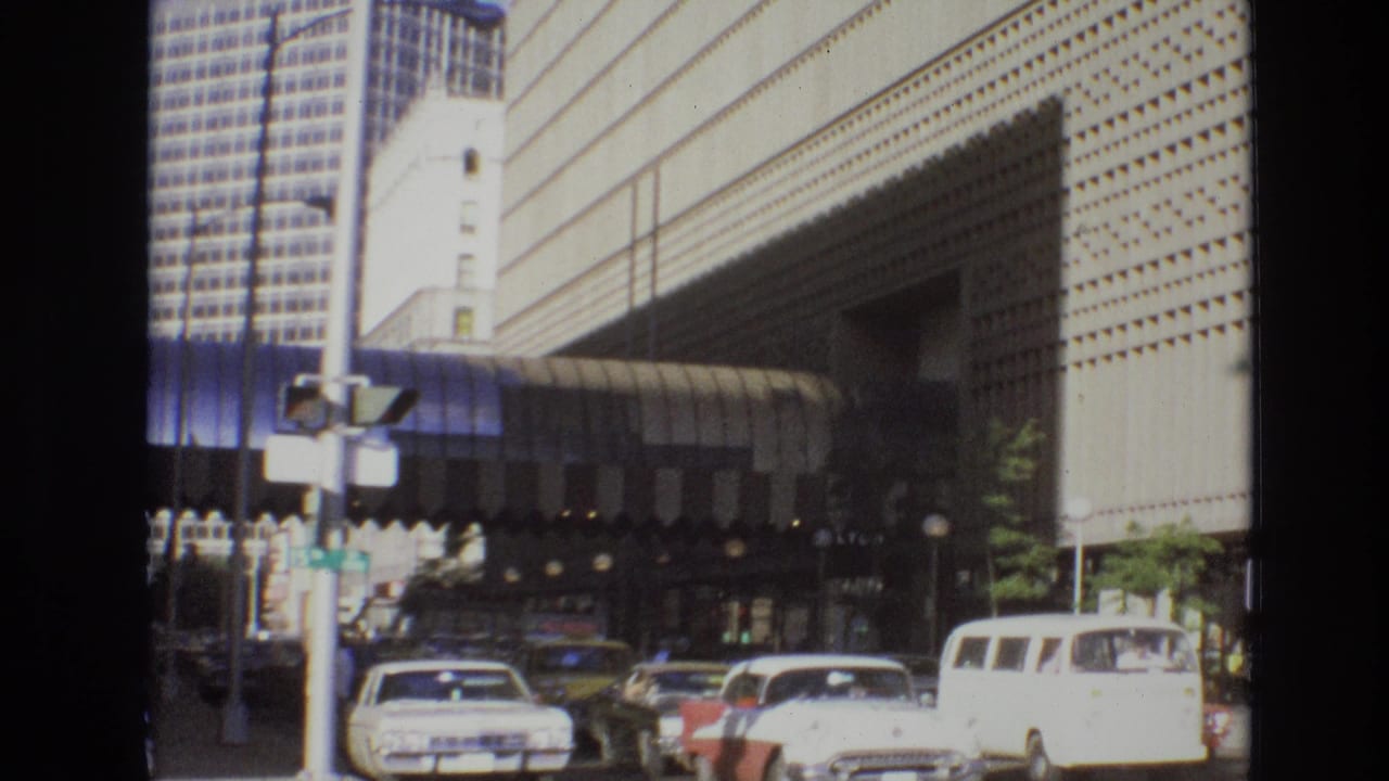 Cars move along a downtown street beside a large building and awning.