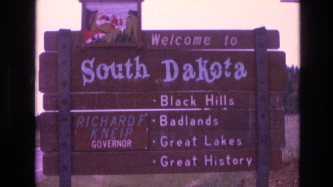 Wooden South Dakota welcome sign with attraction text and dark film border.