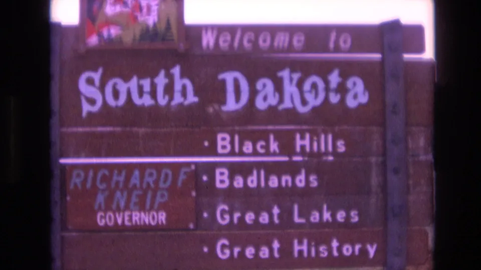 Zoomed-in 1974 view of the South Dakota welcome sign, showing the large state name, Black Hills, Badlands, Great Lakes, and governor name panel.