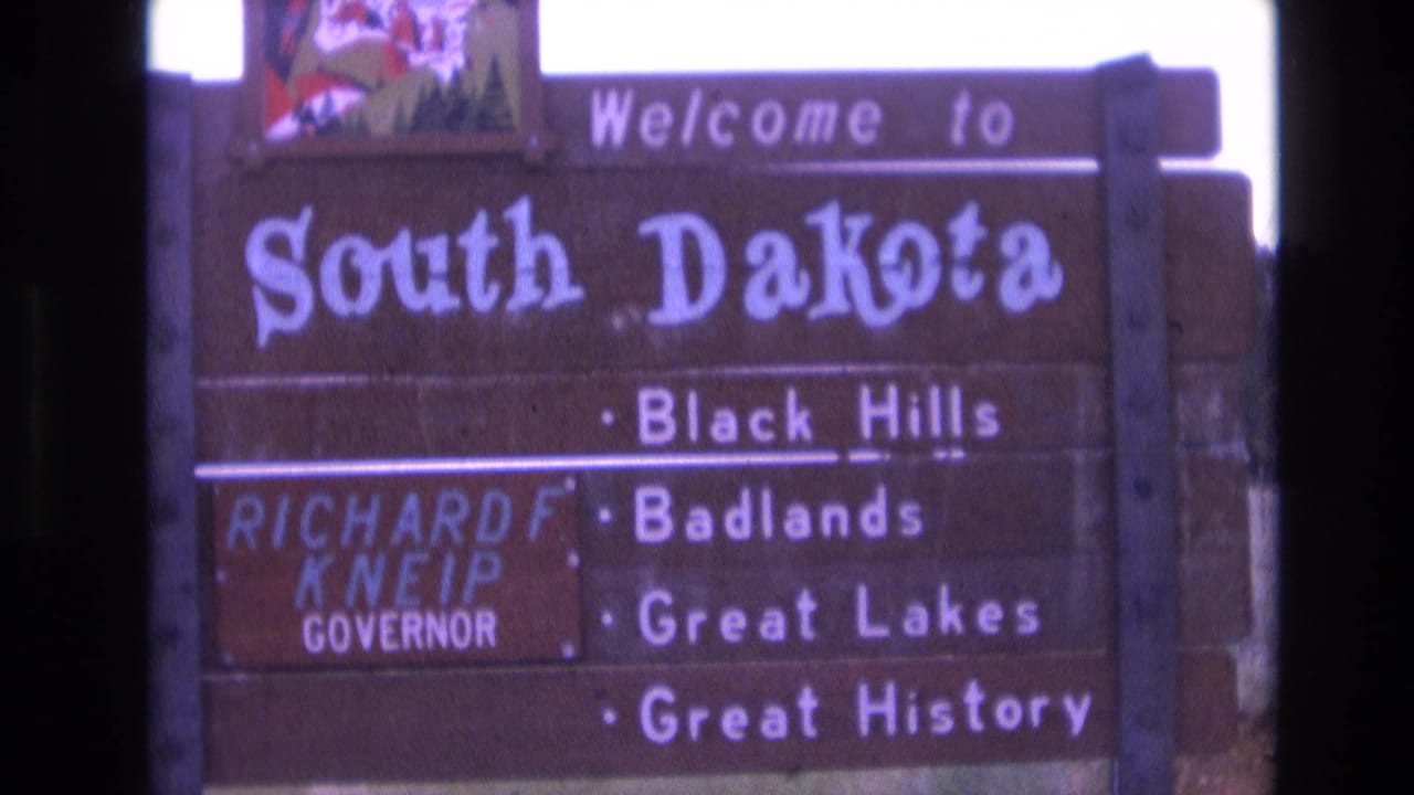 1974 8mm view of the South Dakota roadside welcome sign, with the Governor Kneip panel partly visible and the Black Hills, Badlands, Great Lakes, and Great History lines readable.