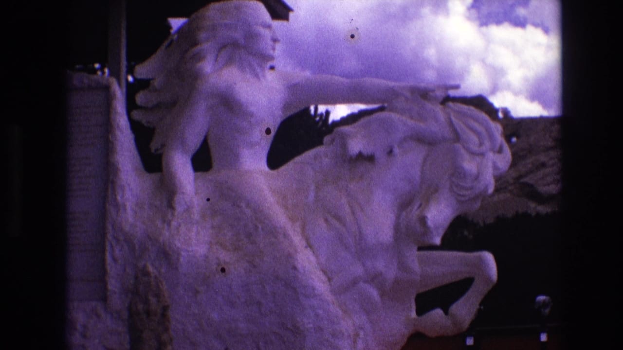 1974 South Dakota 8mm frame showing a white outdoor equestrian sculpture of a long-haired rider pointing forward beside a stone plaque under cloudy sky.