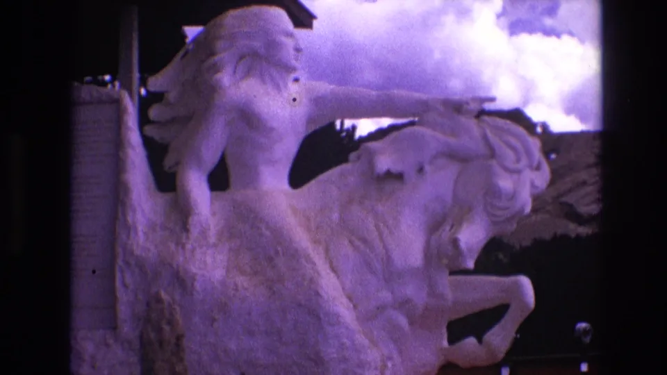 1974 South Dakota 8mm frame showing the same Native American figure on a rearing horse, with the statue partly softened by home-movie focus and color shift.