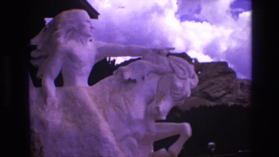 Final 1974 South Dakota frame of the stone Native American rider and rearing horse sculpture, captured as a short tourist cutaway with Super 8 grain and purple sky shift.