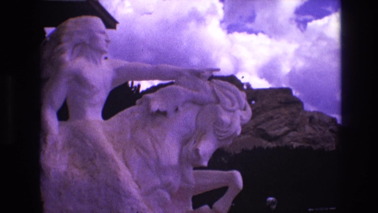 A 1974 South Dakota 8mm frame shows a large white statue of a Native American figure on horseback, with a rocky outcropping and cloud-filled sky behind it.