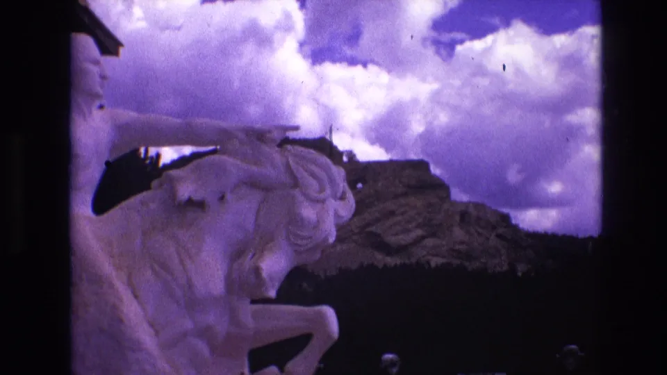 A slightly shifted 8mm frame emphasizes the statue's horse body and pointing rider, with the purple-tinted sky and rugged rock formation filling the background.