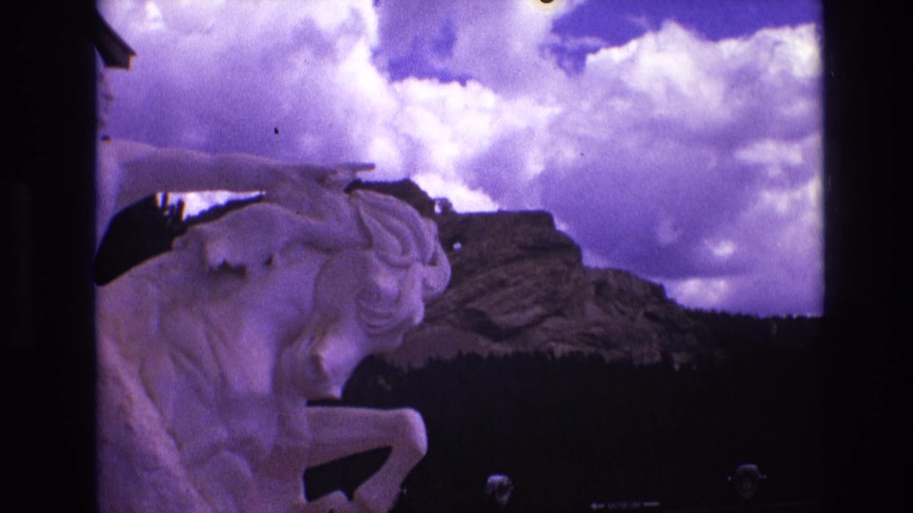 1974 South Dakota 8mm frame showing a white horse statue at left with rocky hills, dark trees, and large clouds in the background.