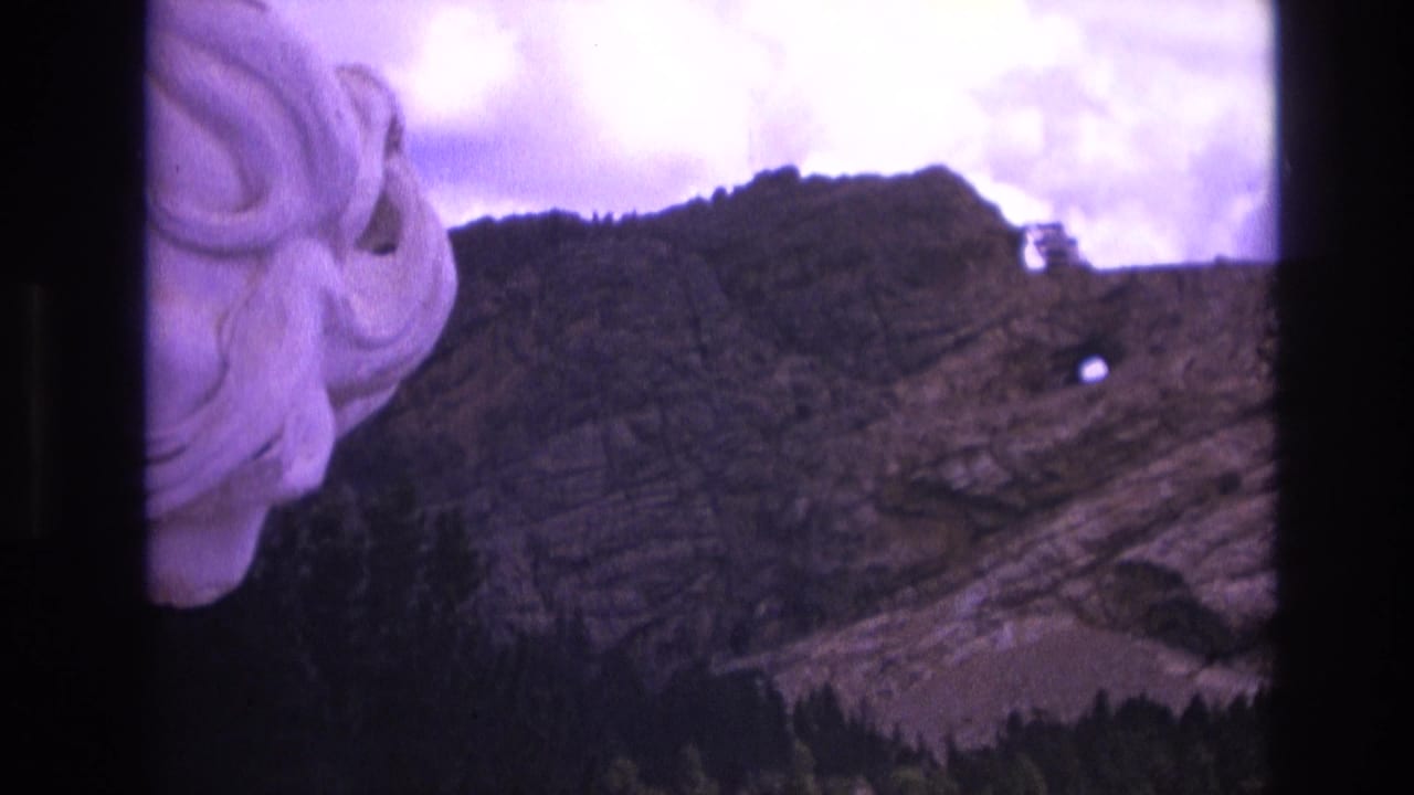 Carved stone face partly visible beside a mountain slope with a small opening in the rock.