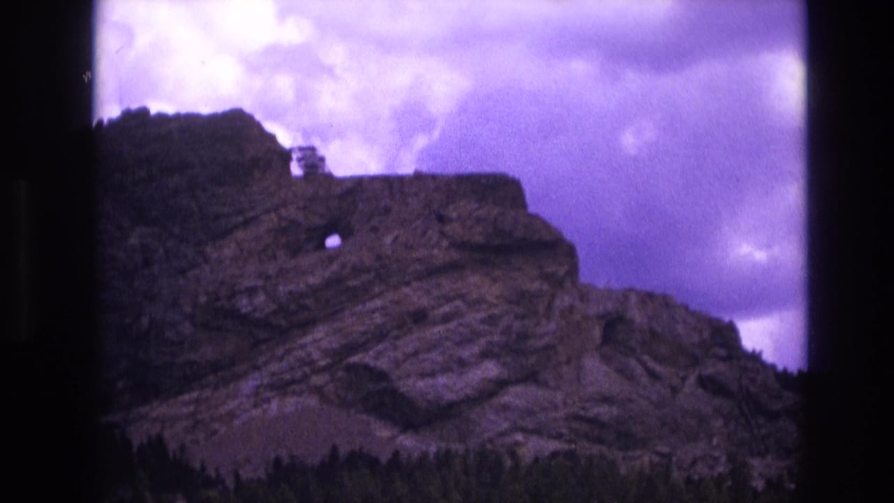 Rocky cliff face with circular opening, dark treeline, and cloudy purple sky.