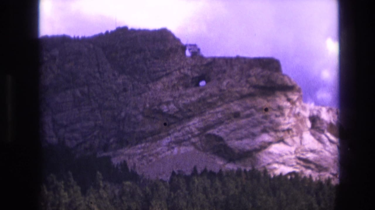 Rock formation and treeline framed by dark film borders and a pale purple sky.