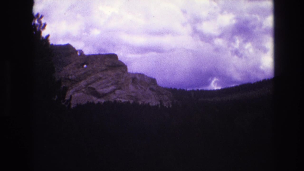 Distant rocky outcrop and forest line beneath a cloudy purple sky.