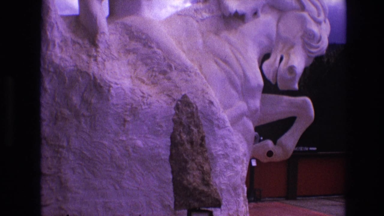 1974 South Dakota 8mm frame showing a close, slightly low view of a white rearing horse sculpture washed in purple light, with a dark pointed object mounted before it.