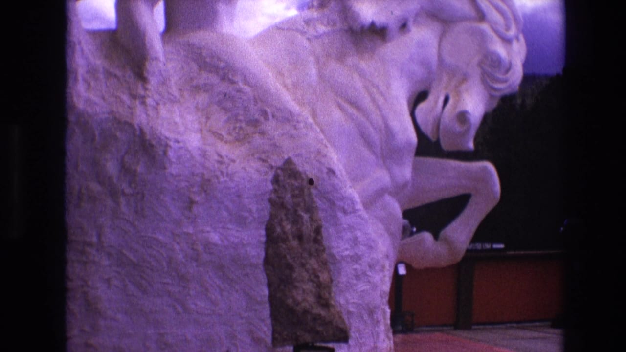 1974 South Dakota frame with the horse sculpture filling most of the view, its rough white stone surface tinted purple against a dark interior display area.