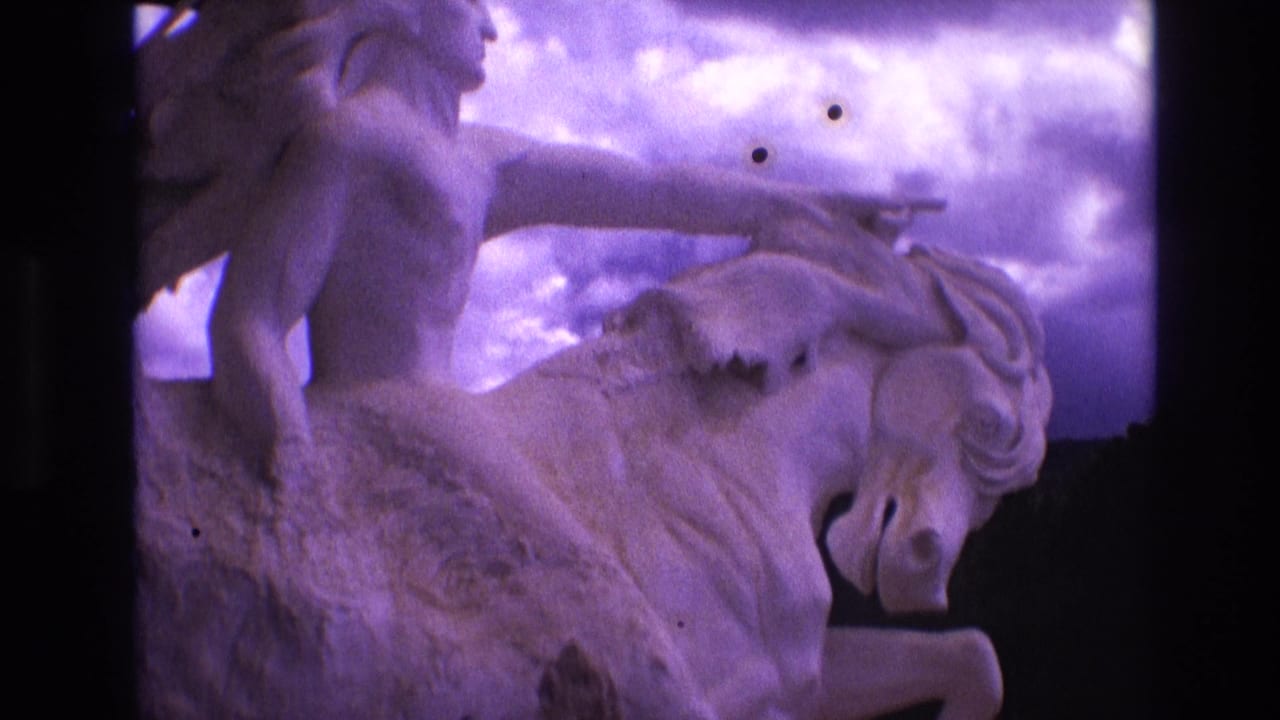 1974 South Dakota 8mm frame showing the mounted male figure and horse sculpture from a slightly wider angle, with clouds behind and purple color fading across the scan.