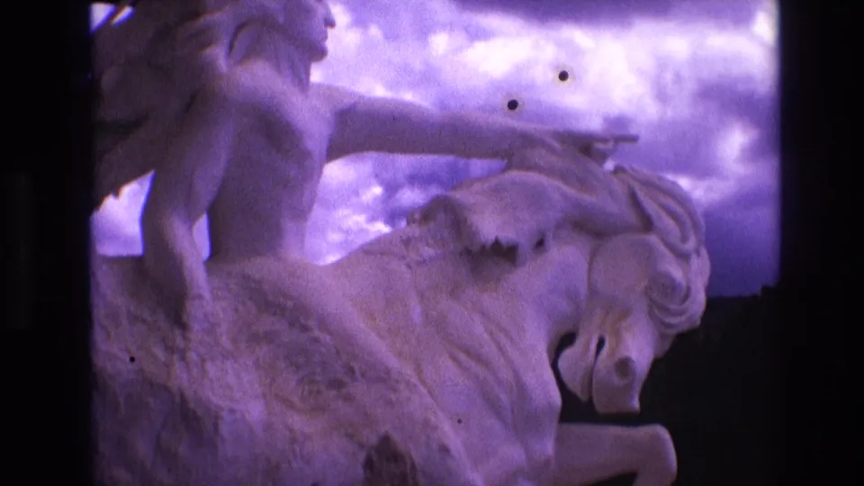 1974 South Dakota 8mm frame showing the mounted male figure and horse sculpture from a slightly wider angle, with clouds behind and purple color fading across the scan.