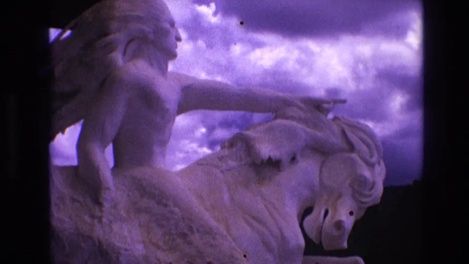 1974 South Dakota 8mm frame showing a side view of the rider's torso and extended arm above the horse's head and neck, with visible grain and a purple-tinted sky.