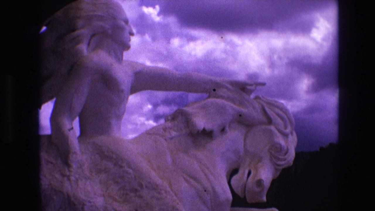 1974 South Dakota 8mm frame showing a pale horse-and-rider statue with a pointing female figure against a purple-tinted cloudy sky.