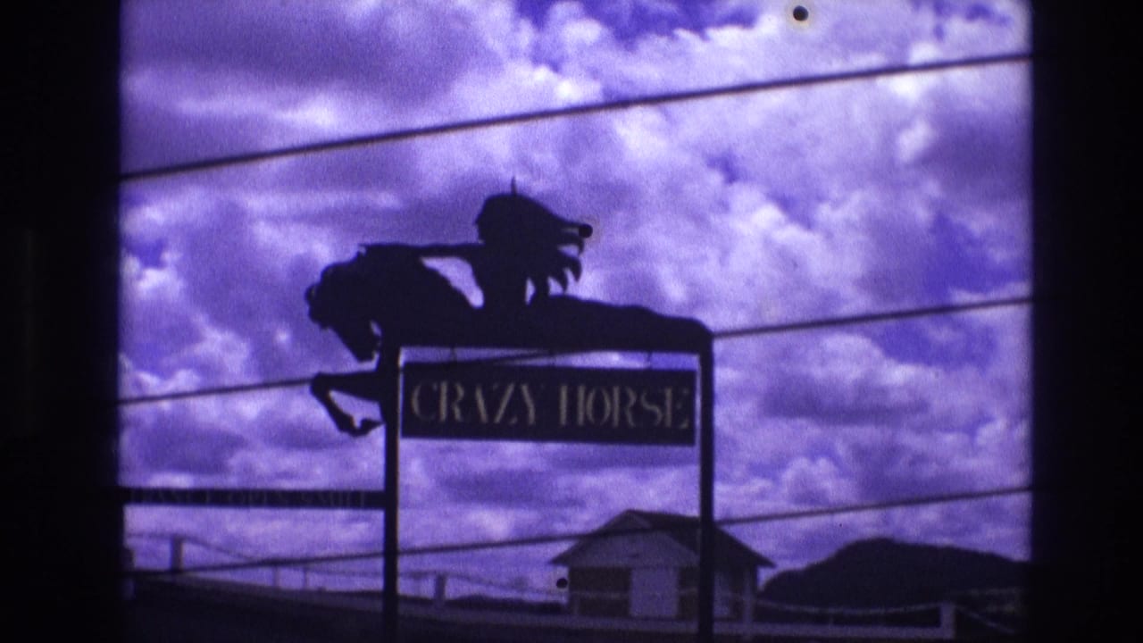 Silhouetted roadside sign reading CRAZY HORSE with rider figure above it.