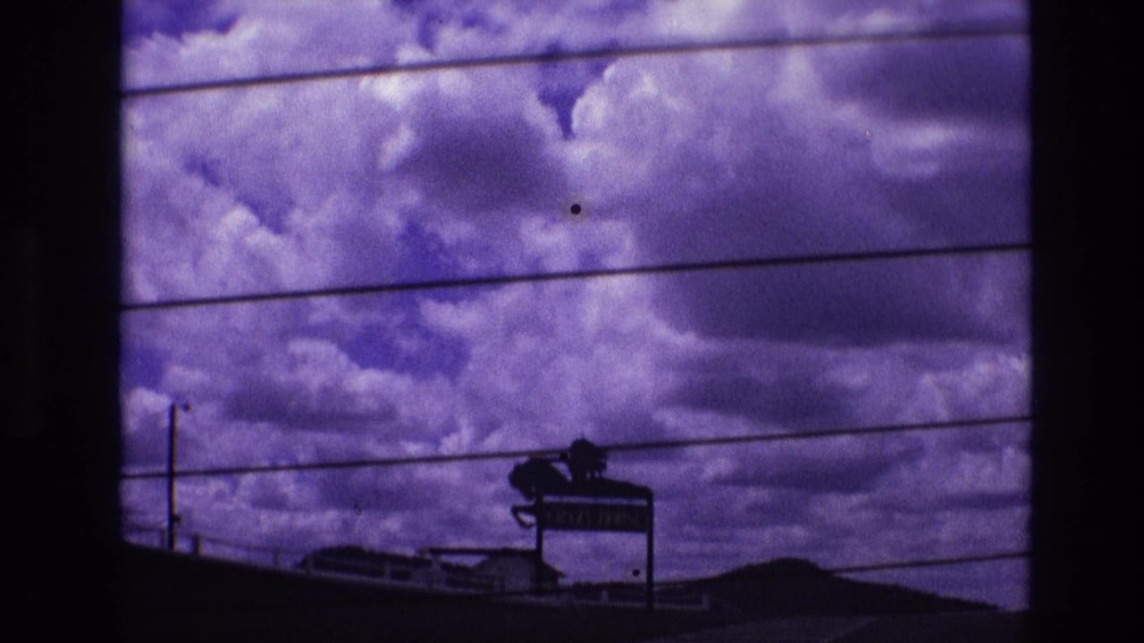 Cloudy sky with horizontal power lines and a dark roadside sign near the lower frame.