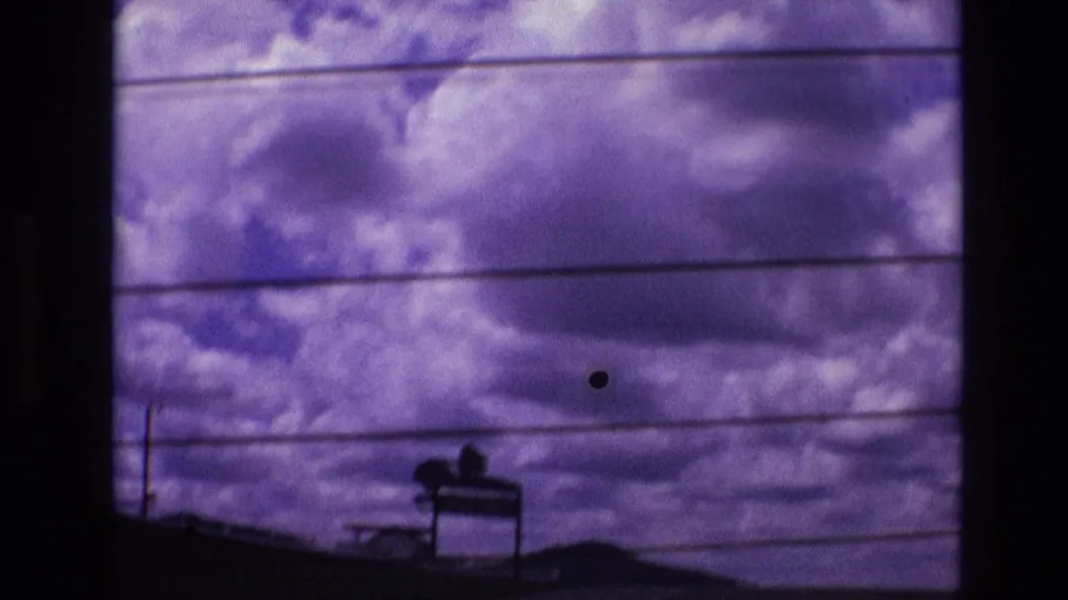 The 8mm frame emphasizes rolling purple-toned clouds and parallel power lines, with a dark roadside sign and low terrain barely visible along the bottom edge.