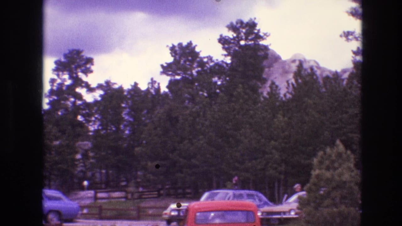 Cars and distant people near a wooded mountain view.