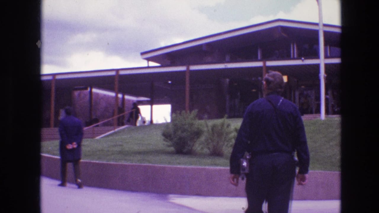 A man walks toward a low modern building while another stands near the path.