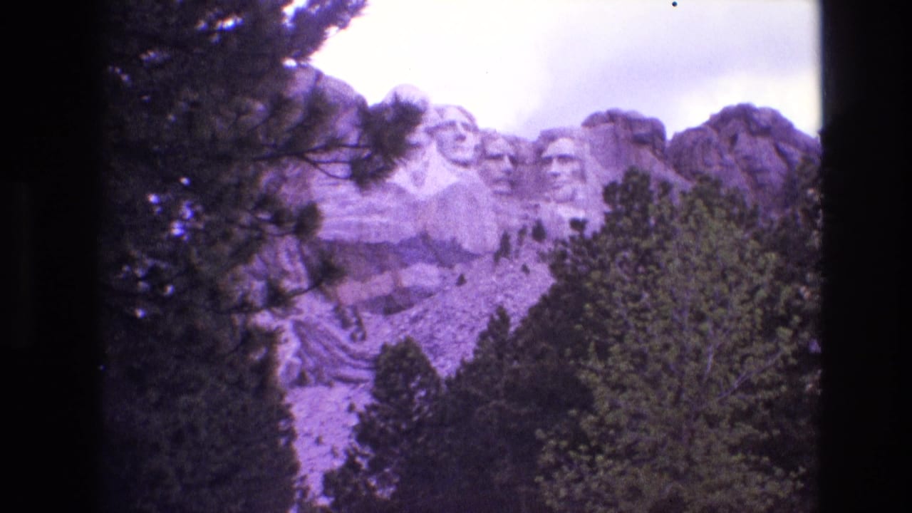 Tree-framed view of Mount Rushmore with the monument partly obscured by foliage.