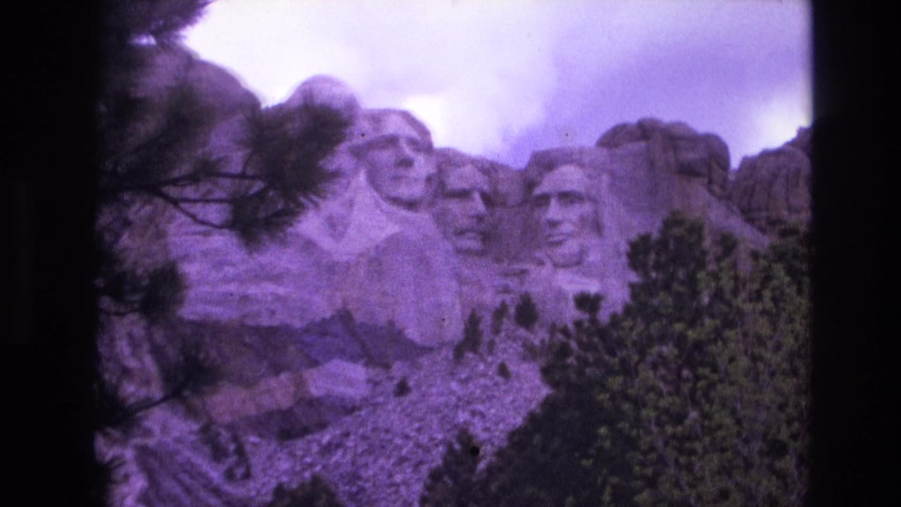 1974 8mm home-movie frame of Mount Rushmore in South Dakota, with the carved presidential heads partly framed by pine branches and a dark film edge.