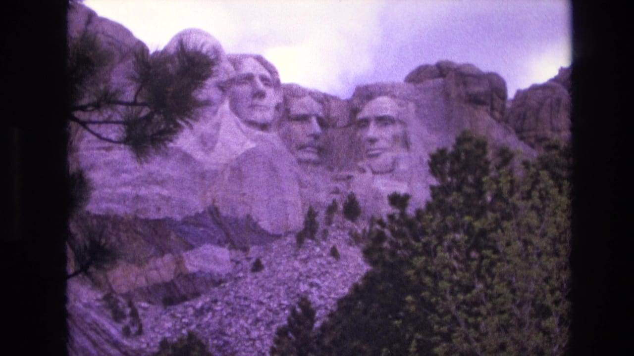 Mount Rushmore sculpture above trees with a rocky slope below.