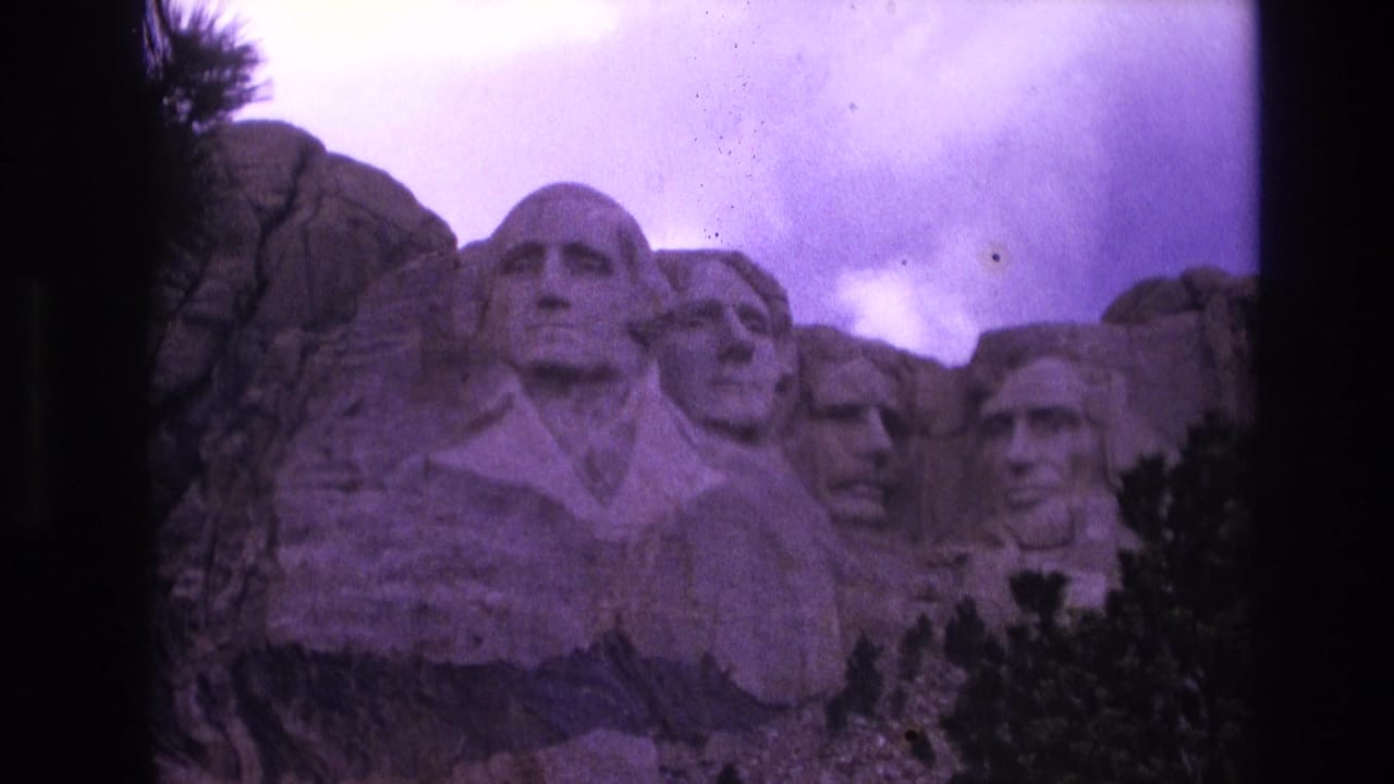 1974 8mm home-movie frame of Mount Rushmore in South Dakota, showing the presidential carvings below a cloudy sky with a purple film cast.